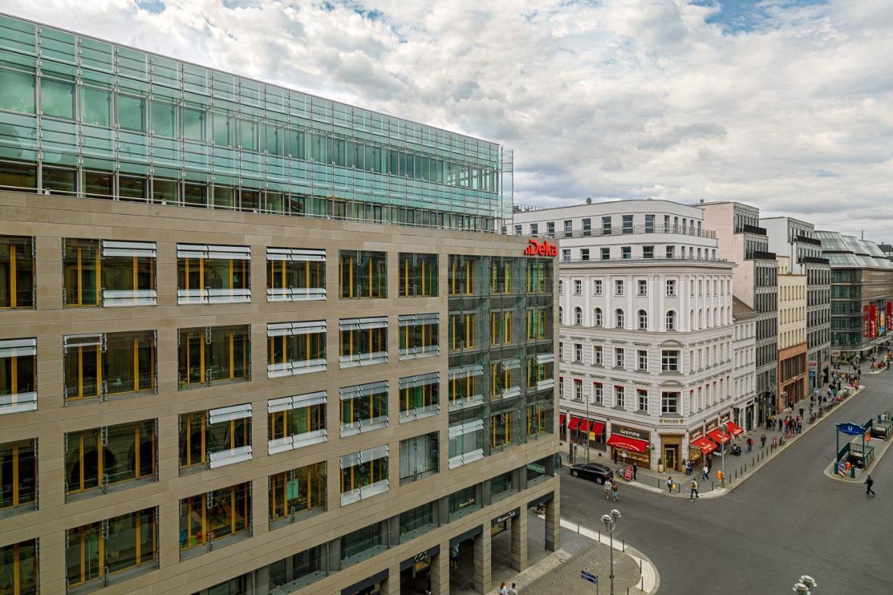 فندق ذا ويستن جراند، برلين المظهر الخارجي الصورة The photo shows an urban scene featuring a modern building on the left side, which has a glass facade and a large entrance, suggesting it may be a commercial or office structure. Adjacent to it, there is another building with traditional architecture