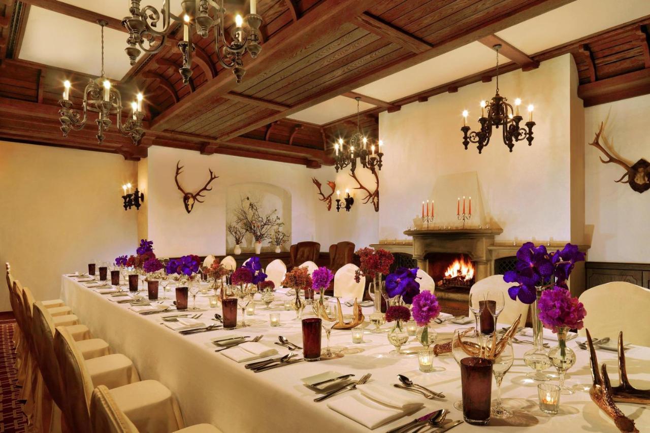 فندق ذا ويستن جراند، برلين المظهر الخارجي الصورة The photo depicts an elegantly arranged dining room. A long table is set with white tablecloths and neatly arranged place settings featuring glassware and cutlery. Vibrant purple flowers are placed in vases at intervals along the table, adding a pop 